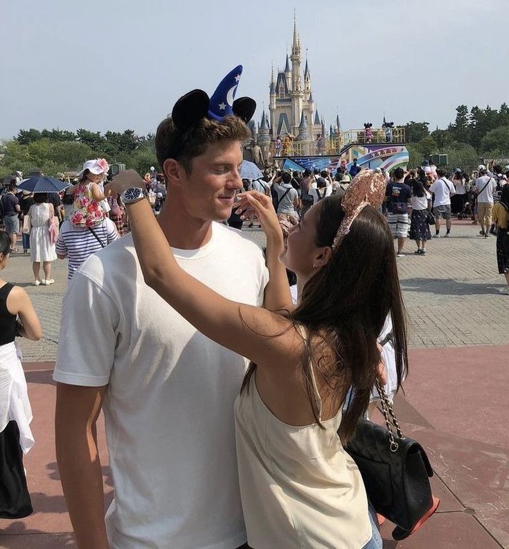 a man and woman standing next to each other in front of a castle at disney world