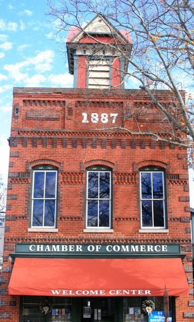 an old brick building with a red awning and clock tower on top that says chamberer of commerge welcome center