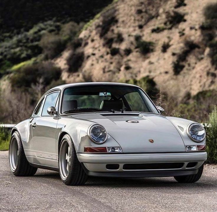 a white porsche parked on the side of a road next to a hill and grass