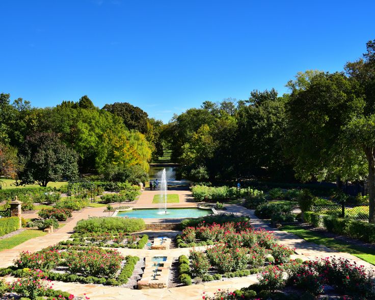 a beautiful garden with a fountain surrounded by greenery and flowers on a sunny day