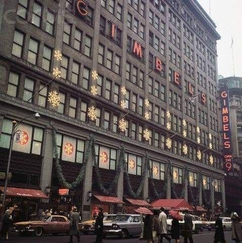 people walking in front of a tall building with christmas decorations on it's windows