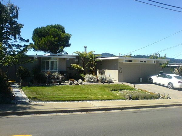 a white car parked in front of a house on the side of a road next to a lush green yard