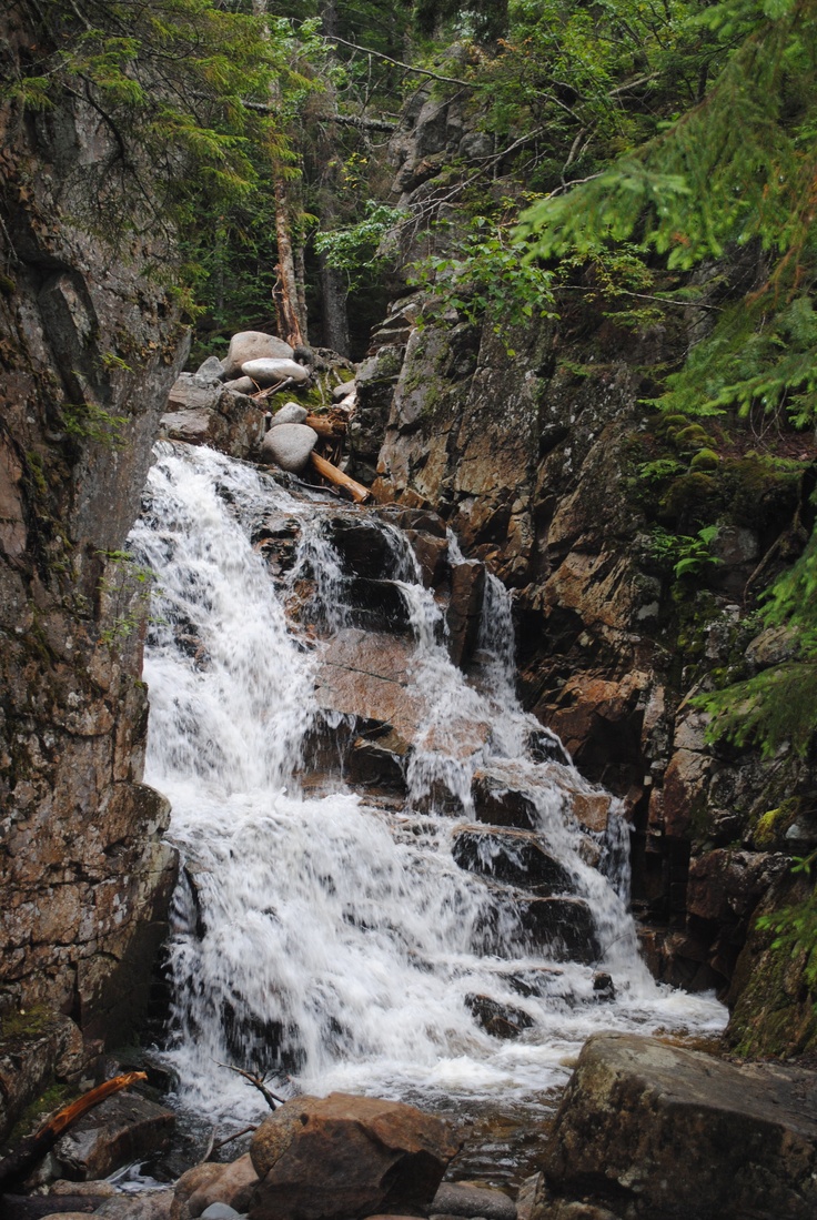 a waterfall in the middle of some rocks and trees with water running down it's sides