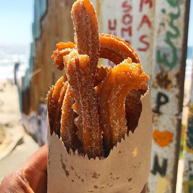 a person holding up a bag full of fried food on the beach in front of an ocean