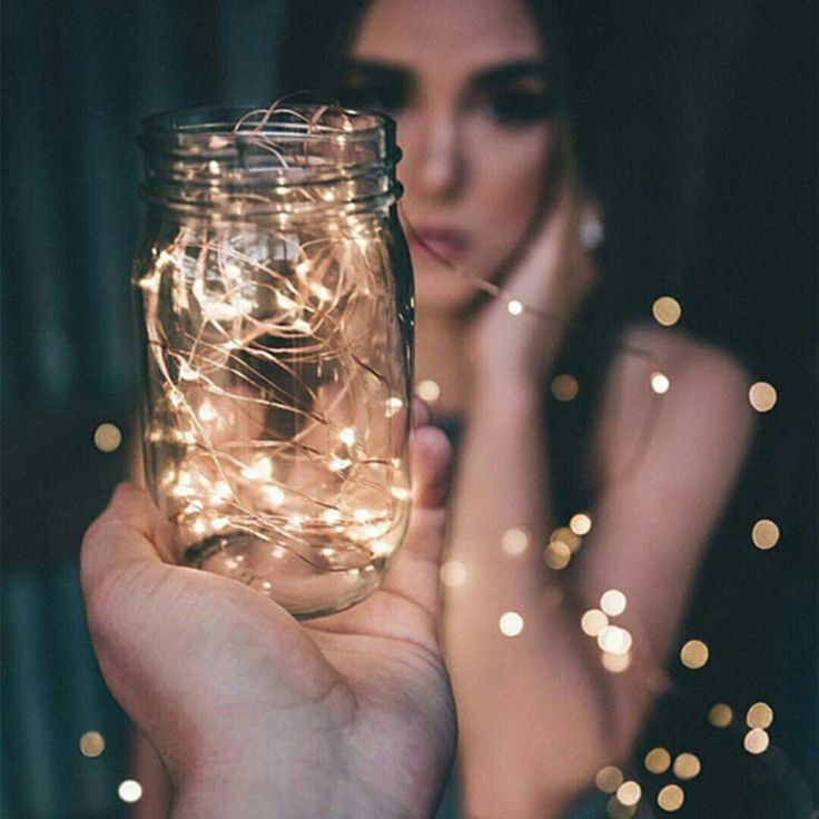 a person holding a mason jar with fairy lights on it in front of their face