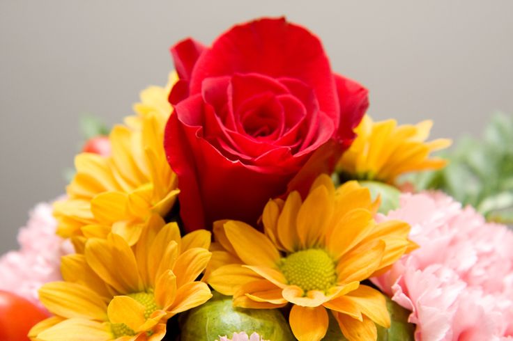 a vase filled with flowers on top of a table next to a red rose and yellow carnations