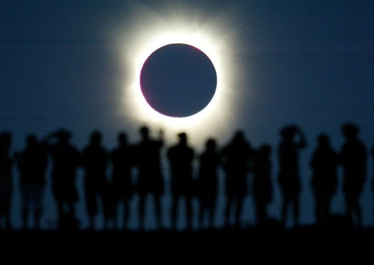 the solar eclipse is seen through silhouettes of people