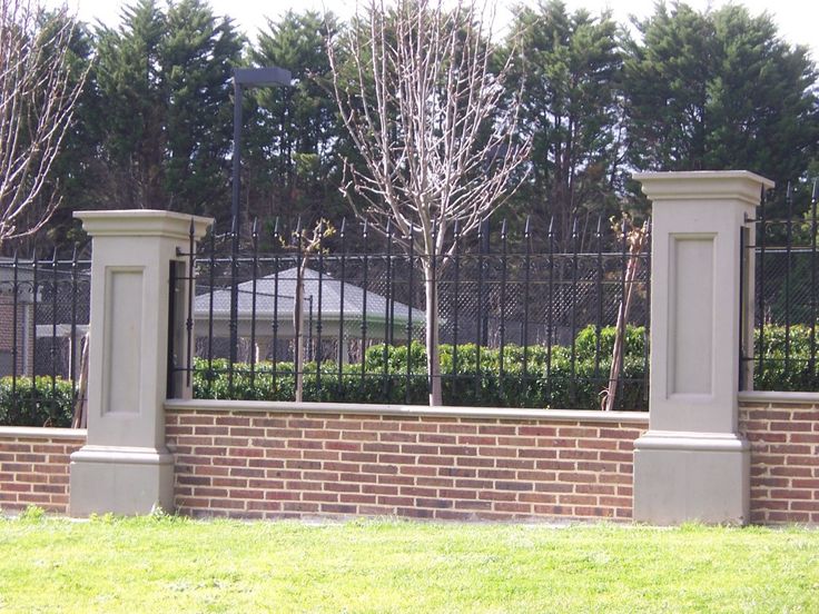 a park bench sitting in front of a brick wall and fence with trees behind it