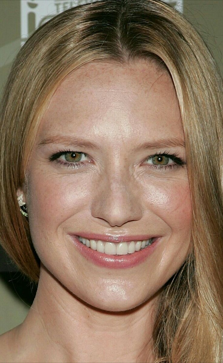 a woman with long blonde hair smiling at the camera and wearing an earring on her left ear