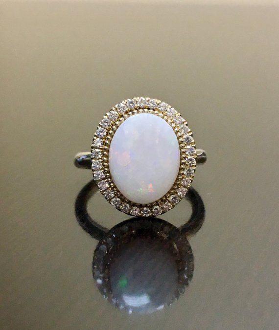 an opal and diamond ring sits on a reflective surface