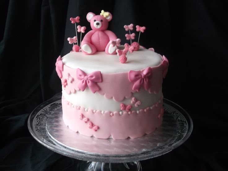 a pink and white decorated cake with a teddy bear on top, sitting on a glass plate