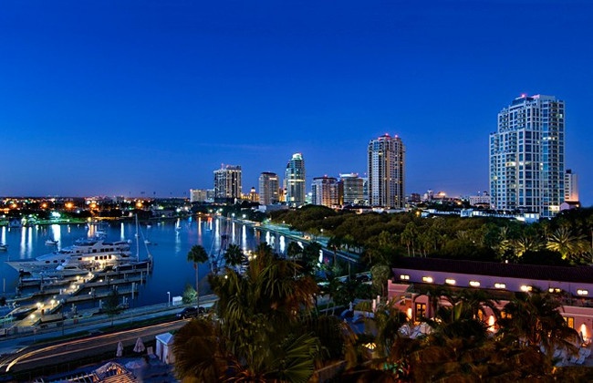 the city skyline is lit up at night with boats in the water and palm trees