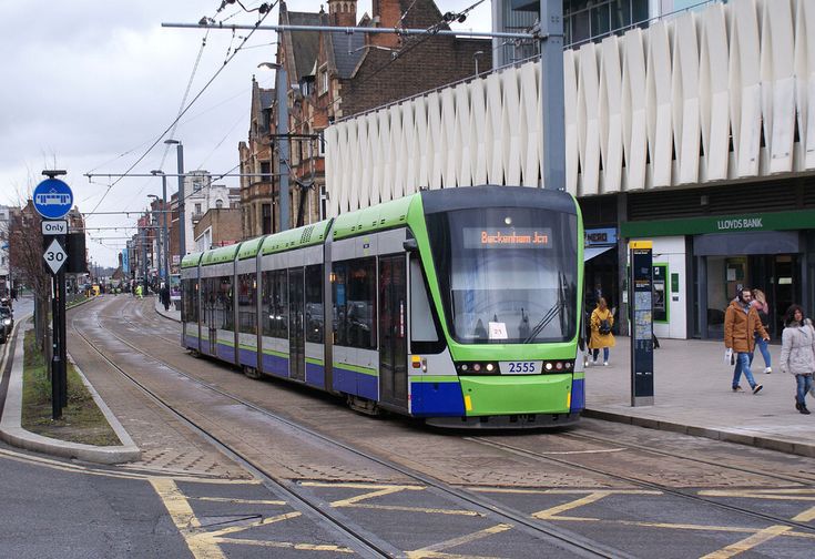 a green and blue train traveling down tracks next to a tall building on a city street