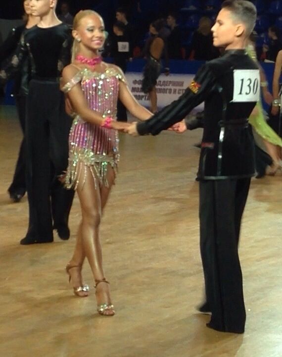 two women shaking hands in front of an audience at a dance competition, with one woman dressed in black and the other wearing a pink beaded dress