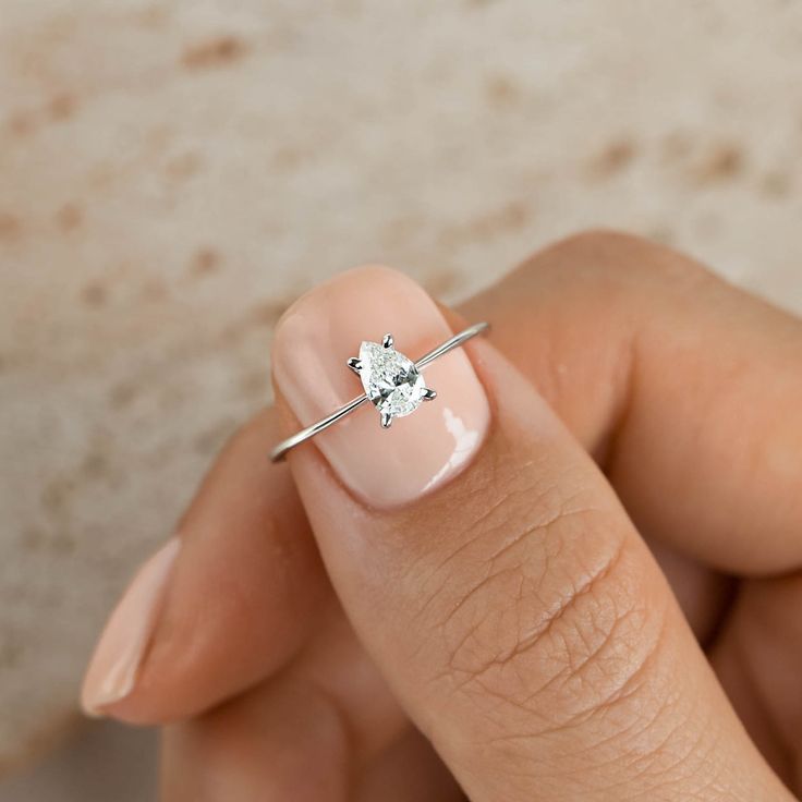 a close up of a person's hand holding a ring with a diamond on it