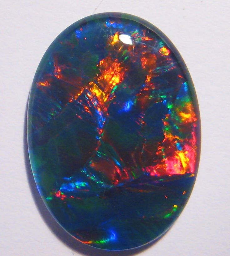 an oval shaped black opal with multicolored lights in the center, on a white background