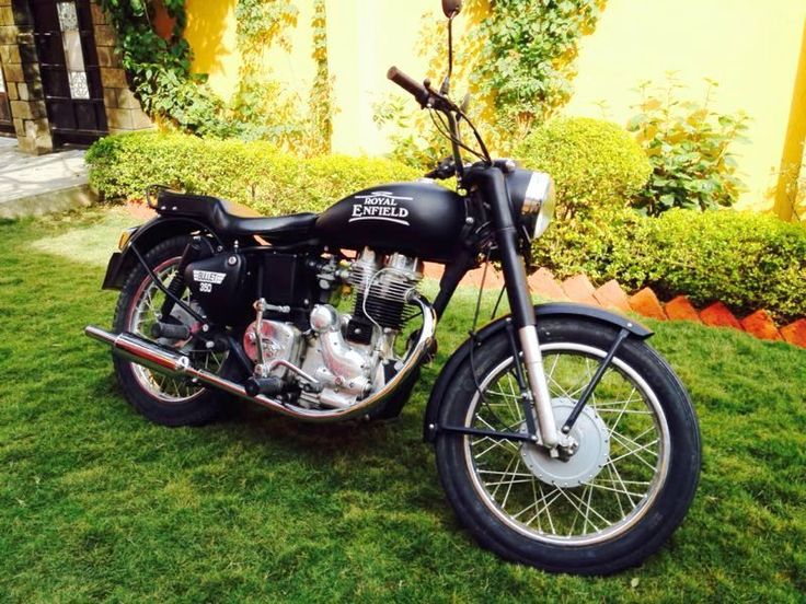 a black motorcycle parked on top of a lush green field next to a yellow building