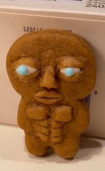 a close up of a cookie shaped like a person with eyes and hands on his chest