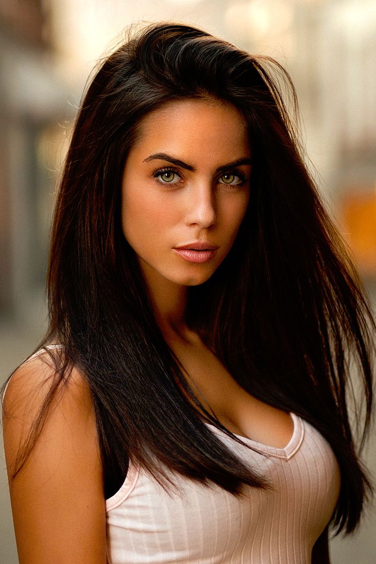 a woman with long black hair posing for the camera, wearing a white tank top