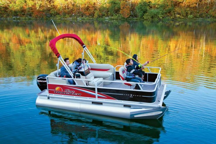 two men fishing on a pontoon boat in the water with fall foliage behind them