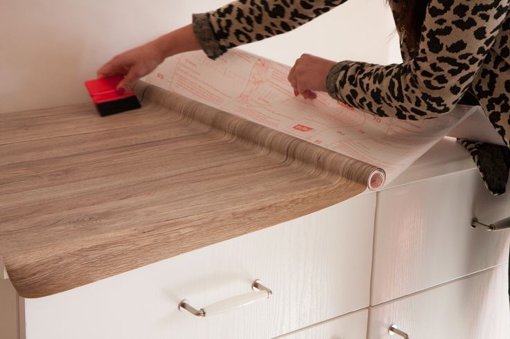 a woman in leopard print shirt holding a red object on top of a white dresser