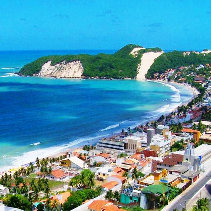 an aerial view of the beach and ocean with houses on it's sides, surrounded by green hills