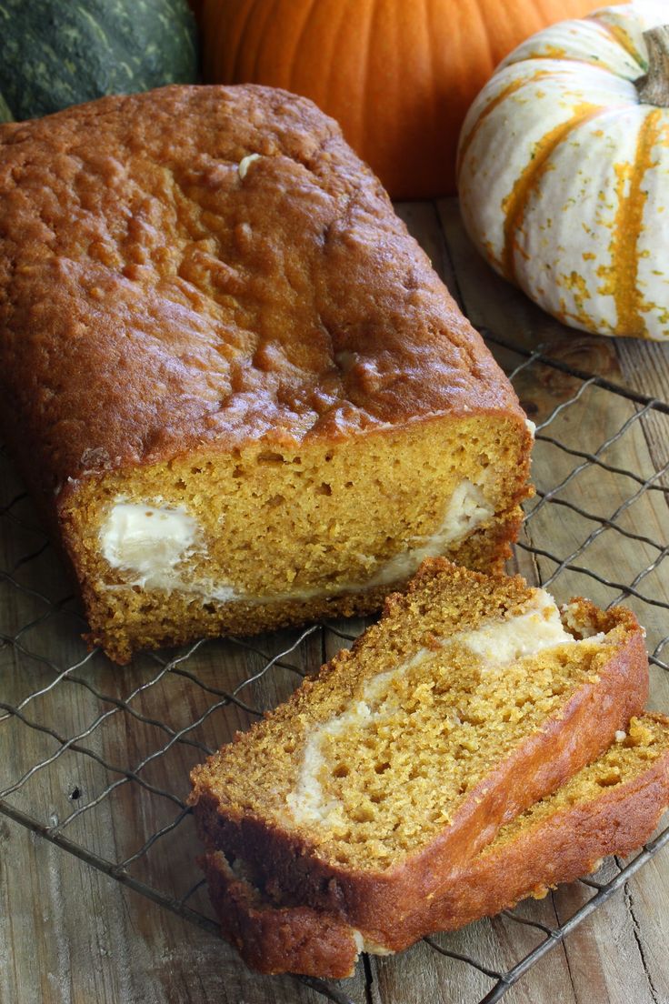 a loaf of pumpkin bread sitting on top of a wire rack next to two pumpkins