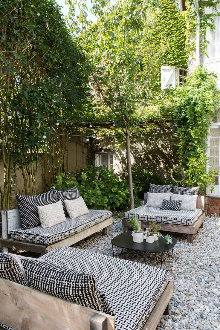 an outdoor living area with couches, tables and trees in the back yard on graveled stones