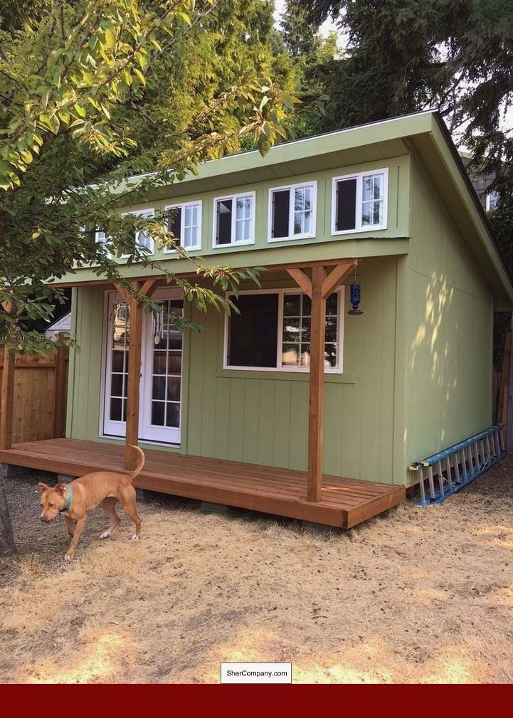 a small green house sitting in the middle of a yard with a dog walking by it