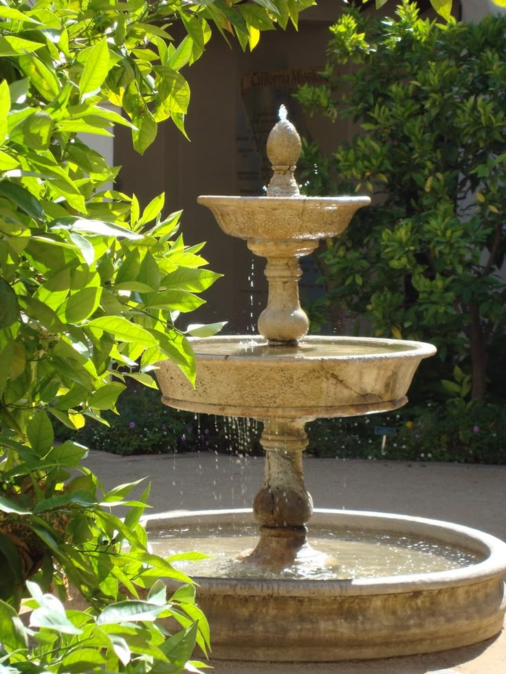 a water fountain surrounded by greenery in the middle of a courtyard area with trees and bushes