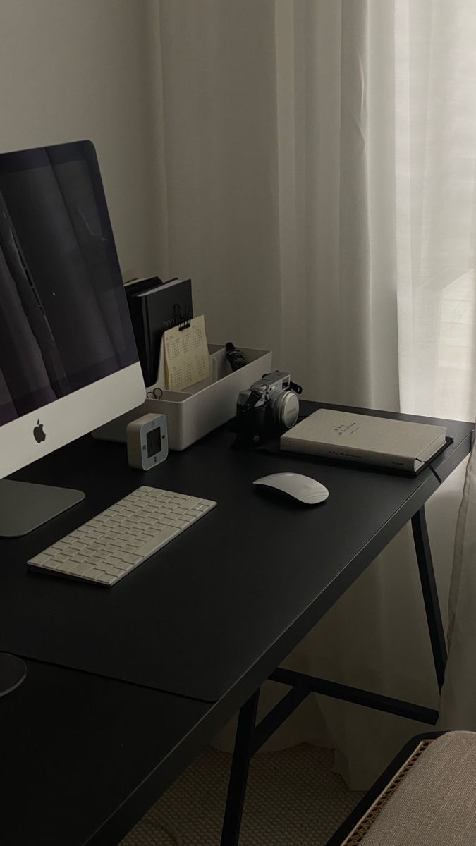 an apple desktop computer sitting on top of a black desk next to a white curtain