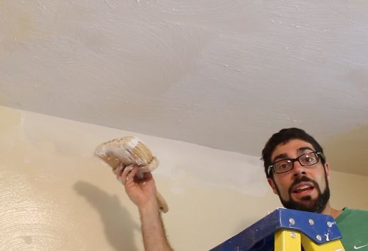 a man is painting the ceiling with white paint and holding an item in his hand