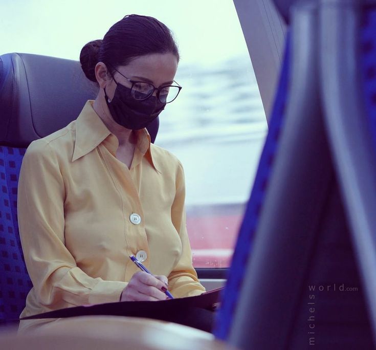 a woman wearing a face mask while sitting in an airplane with a notebook and pen