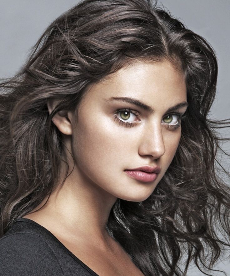 a beautiful young woman with long hair posing for a photo in front of a gray background