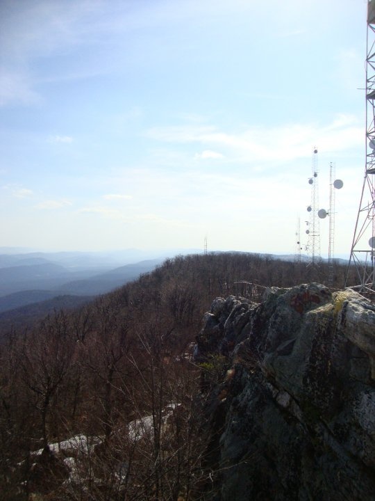 a cell phone tower sitting on top of a rocky hill next to a tree covered hillside