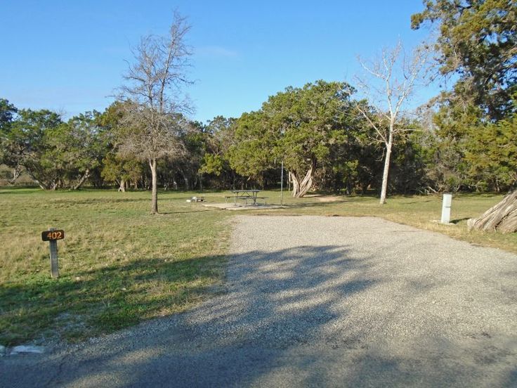 a dirt road in the middle of a grassy field with trees and picnic tables behind it