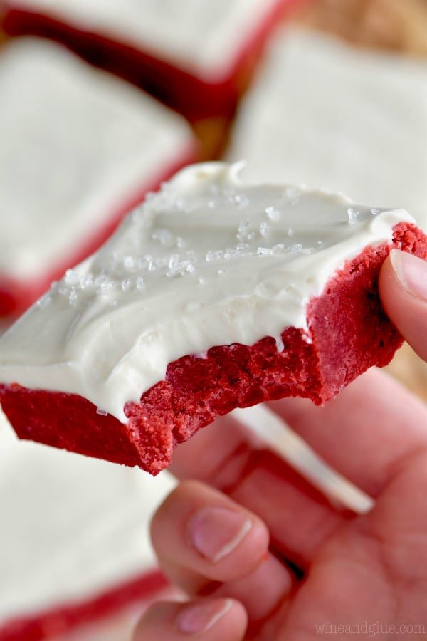 a hand holding a piece of red velvet cake with white frosting on it's end