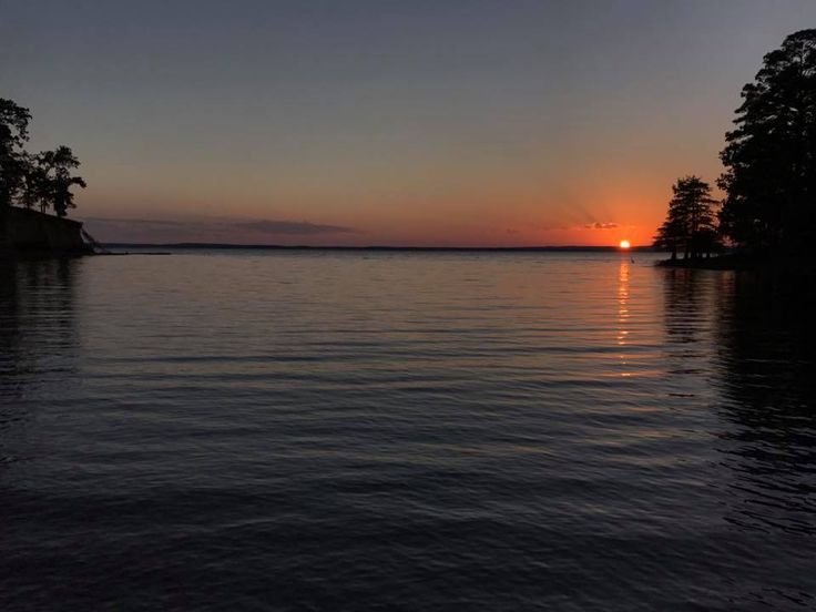 the sun is setting over water with trees in the foreground