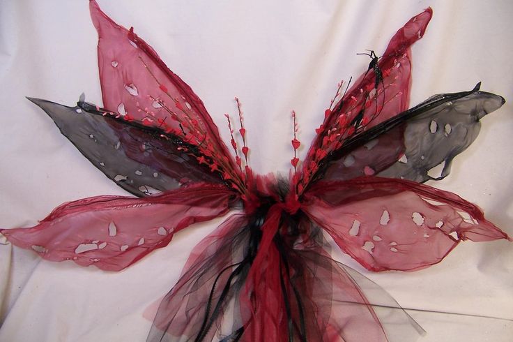 a red and black butterfly made out of organe netting on a white sheeted surface