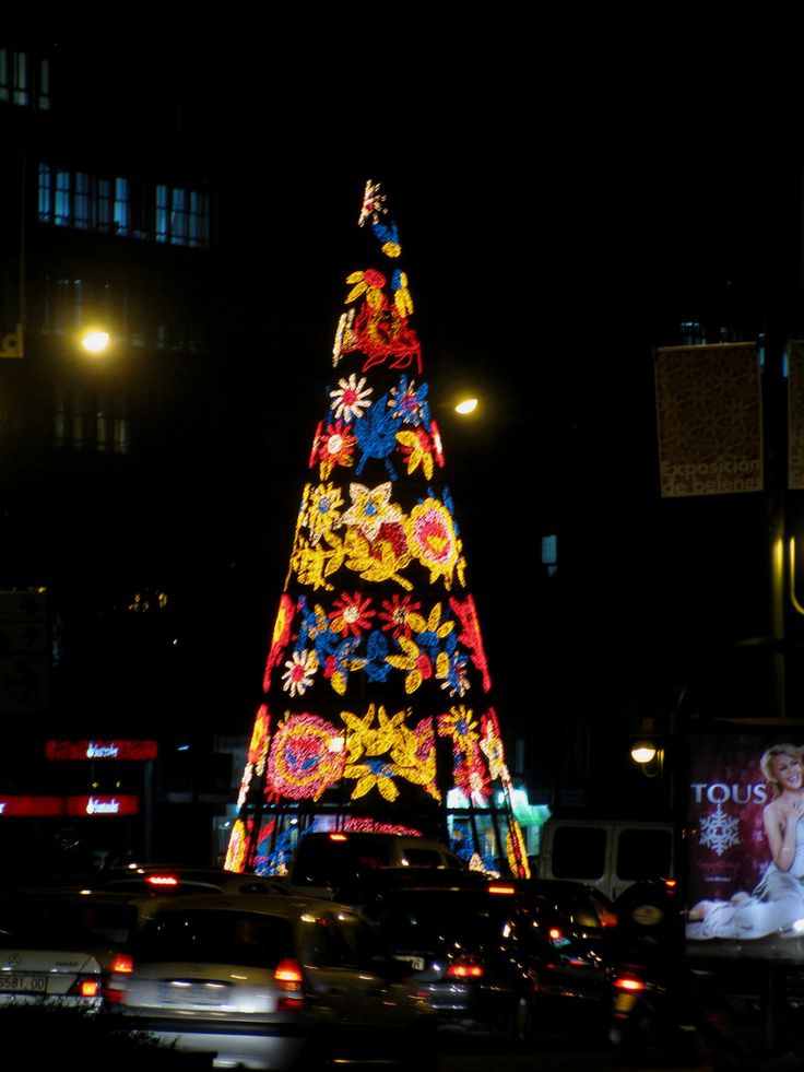 a christmas tree is lit up in the middle of a busy city street at night