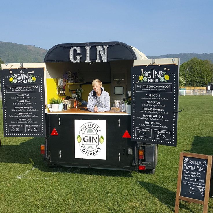 a man behind the counter of a gin truck on display in a field with chalkboard signs