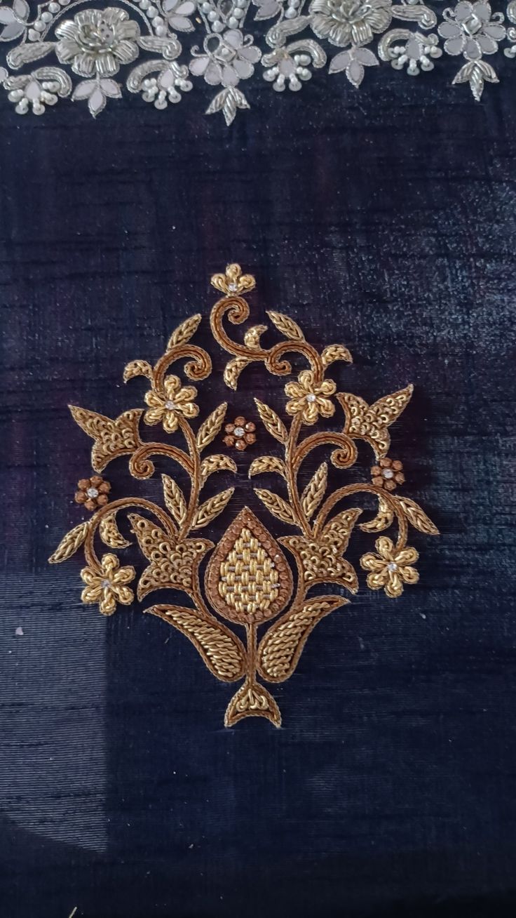 an embroidered piece with gold and silver flowers on it's side, in front of a black background