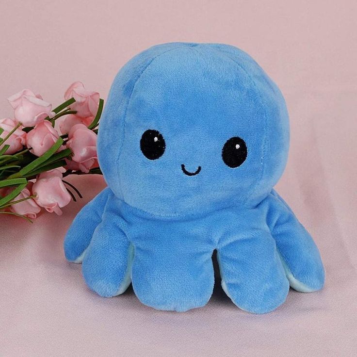 a blue octopus stuffed animal next to pink flowers on a white surface with light pink background