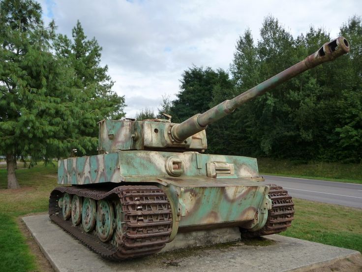 an old rusted tank sitting on top of a cement block in front of trees