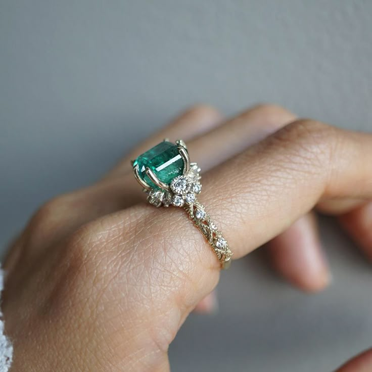 a woman's hand wearing a ring with an emerald and white diamond center stone