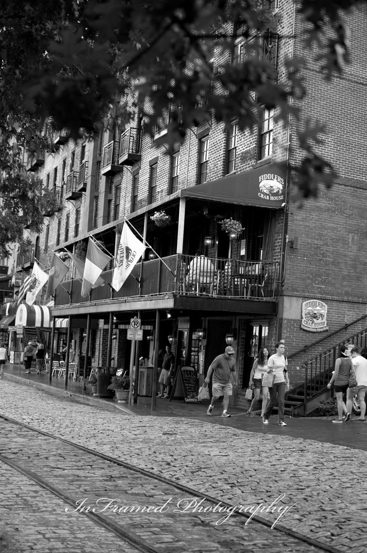 black and white photograph of people walking in front of an old brick building on a cobblestone street