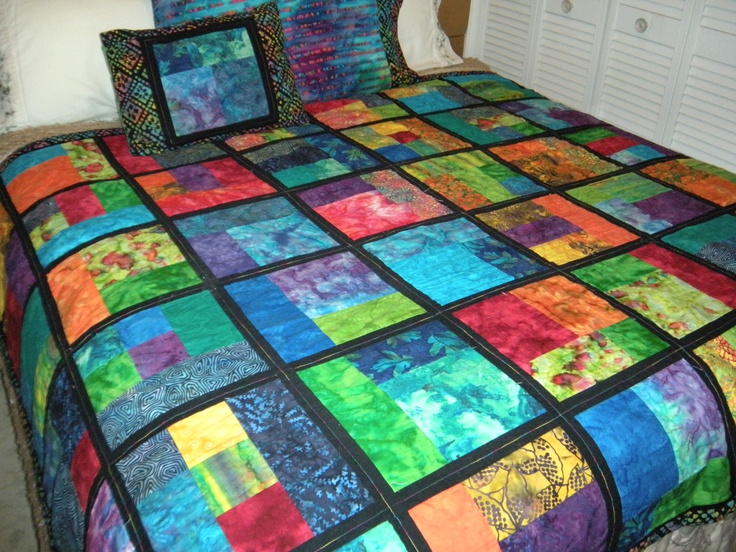 a multicolored quilt on a bed in a room with white walls and drawers