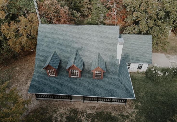 an aerial view of a house with three dormers on the roof and trees in the background