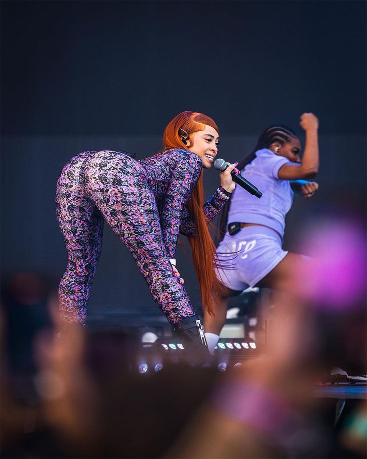 two women are performing on stage with one holding a microphone and the other standing up