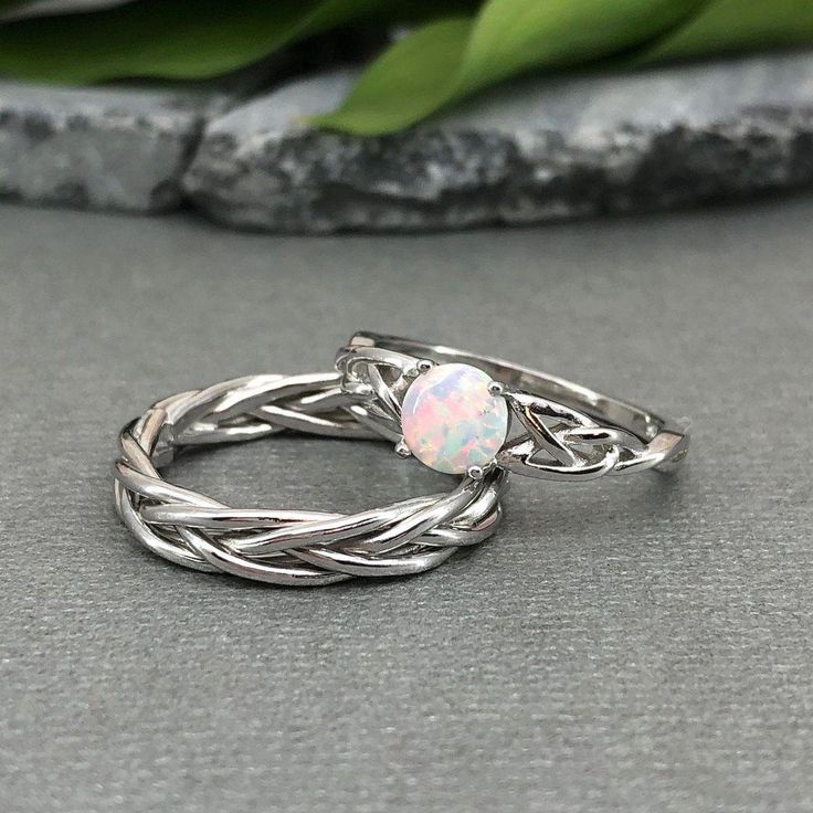 two silver rings with an opal stone in the center on top of a gray surface